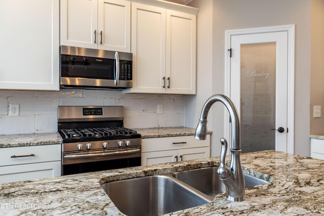 kitchen featuring appliances with stainless steel finishes, white cabinetry, sink, decorative backsplash, and light stone counters