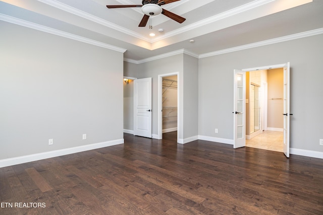 unfurnished bedroom with ensuite bathroom, crown molding, a spacious closet, a tray ceiling, and dark hardwood / wood-style flooring