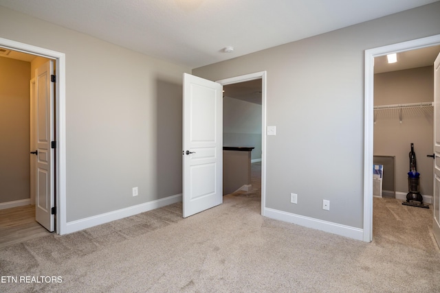 unfurnished bedroom featuring a spacious closet, light carpet, and a closet