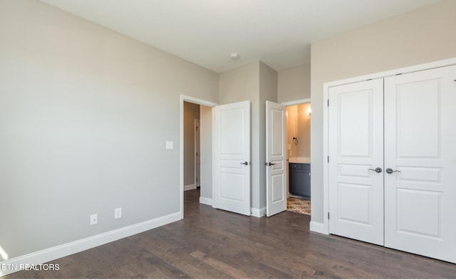 unfurnished bedroom featuring ensuite bath, dark hardwood / wood-style flooring, and a closet