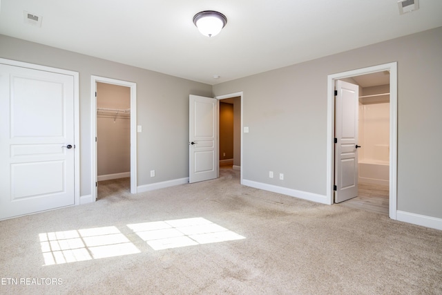 unfurnished bedroom featuring light carpet, ensuite bath, a walk in closet, and a closet