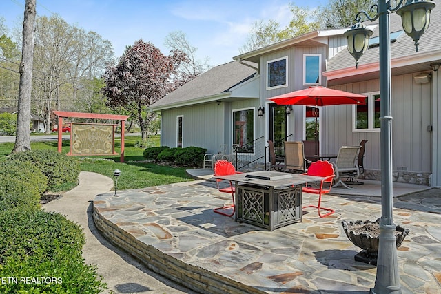 rear view of house featuring a patio, a fire pit, roof with shingles, and a lawn