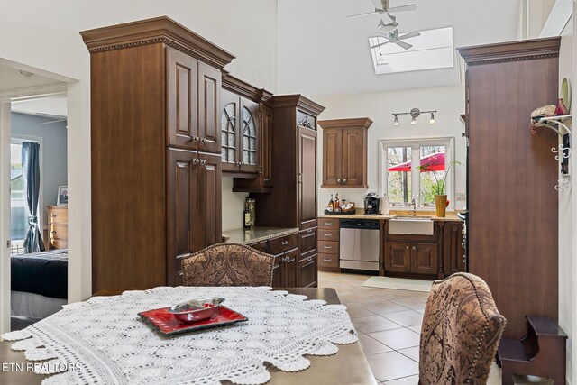 kitchen featuring light tile patterned floors, a skylight, a sink, dark brown cabinets, and dishwasher