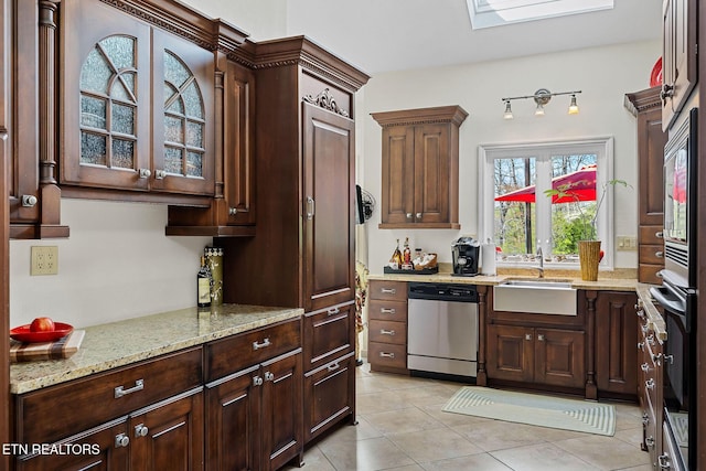 kitchen with a sink, a skylight, glass insert cabinets, light stone countertops, and dishwasher