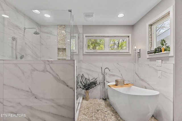 bathroom with a soaking tub, a healthy amount of sunlight, tile walls, and a marble finish shower