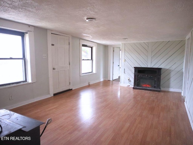 unfurnished living room featuring hardwood / wood-style flooring, wooden walls, and a textured ceiling