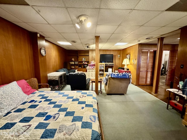 carpeted bedroom with a drop ceiling and wood walls