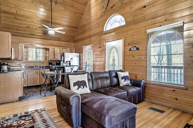 living room featuring sink, wood walls, high vaulted ceiling, ceiling fan, and light hardwood / wood-style floors