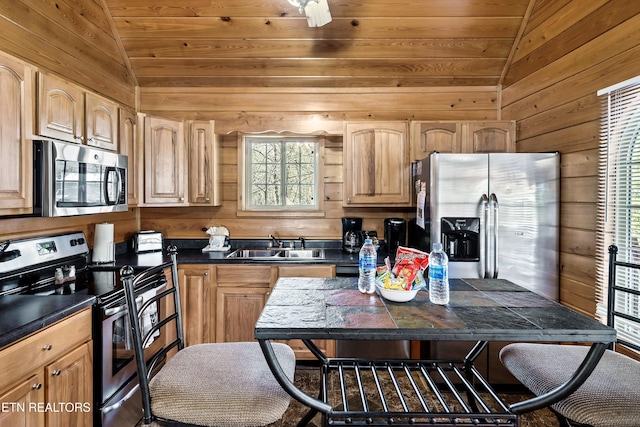 kitchen with stainless steel appliances, vaulted ceiling, sink, and wood walls