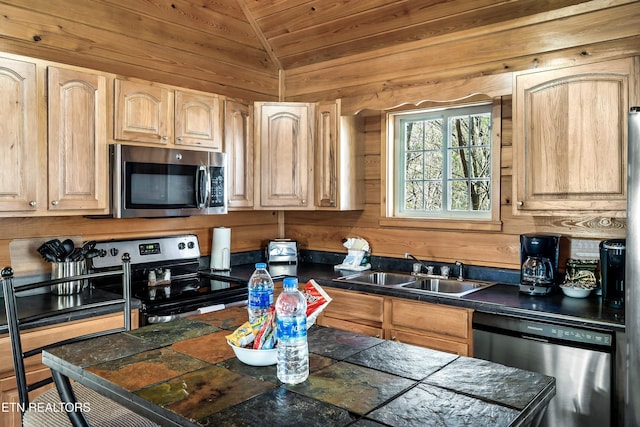 kitchen featuring light brown cabinetry, sink, vaulted ceiling, wooden walls, and stainless steel appliances