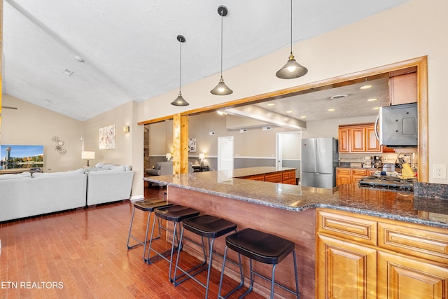 kitchen featuring dark stone countertops, a breakfast bar area, stainless steel refrigerator, and decorative light fixtures