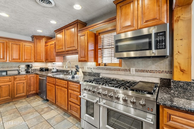 kitchen featuring backsplash, stainless steel appliances, sink, and dark stone counters