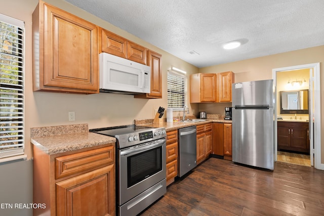 kitchen with light stone counters, appliances with stainless steel finishes, dark hardwood / wood-style floors, and sink