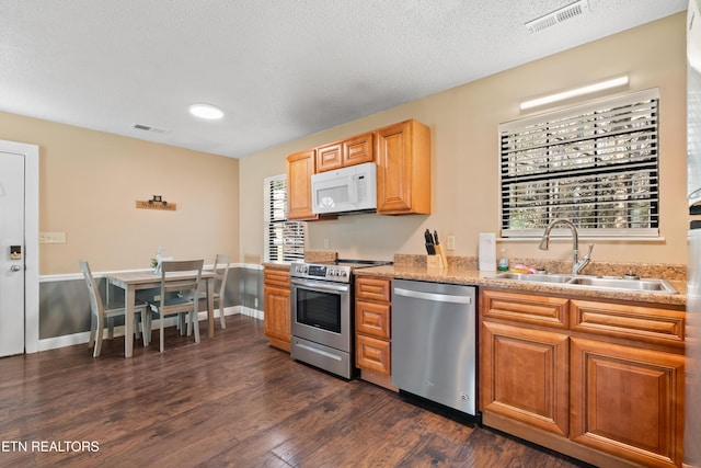 kitchen with appliances with stainless steel finishes, sink, a textured ceiling, and dark hardwood / wood-style flooring