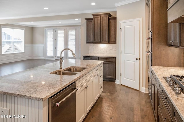 kitchen featuring light stone counters, appliances with stainless steel finishes, dark wood-type flooring, a kitchen island with sink, and a sink