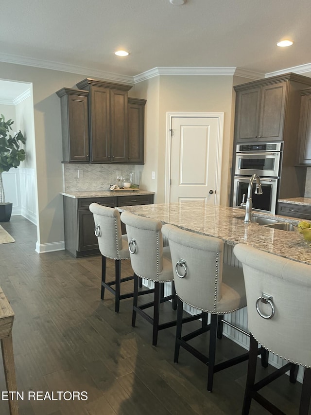 kitchen featuring dark wood-style flooring, a sink, ornamental molding, tasteful backsplash, and a kitchen bar