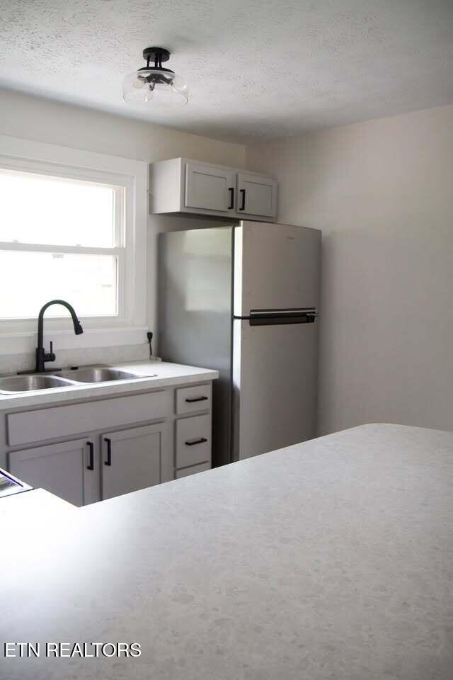 kitchen with white cabinetry, sink, stainless steel fridge, and a textured ceiling