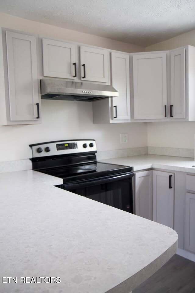 kitchen with black range with electric stovetop, white cabinets, and a textured ceiling