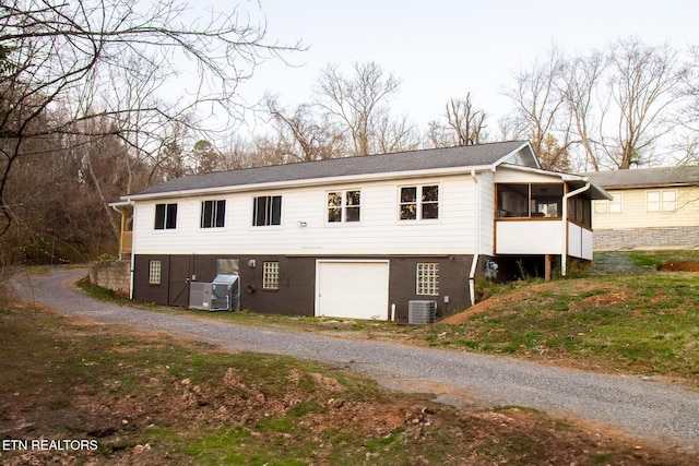 view of front facade with gravel driveway, central air condition unit, a garage, and a sunroom