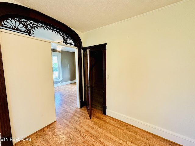 hall with light hardwood / wood-style flooring, ornamental molding, and a textured ceiling