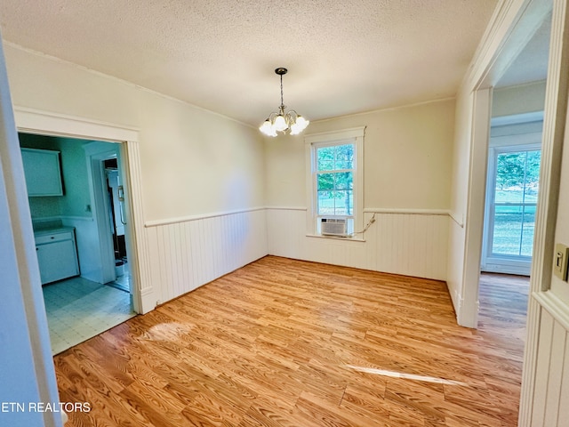 unfurnished dining area with an inviting chandelier, hardwood / wood-style floors, a textured ceiling, and cooling unit