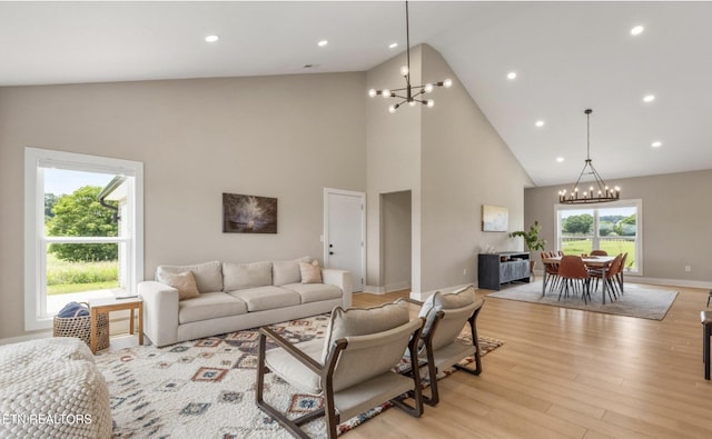 living room featuring plenty of natural light, high vaulted ceiling, an inviting chandelier, and light hardwood / wood-style flooring