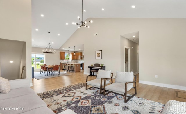 living room with a notable chandelier, high vaulted ceiling, and light wood-type flooring