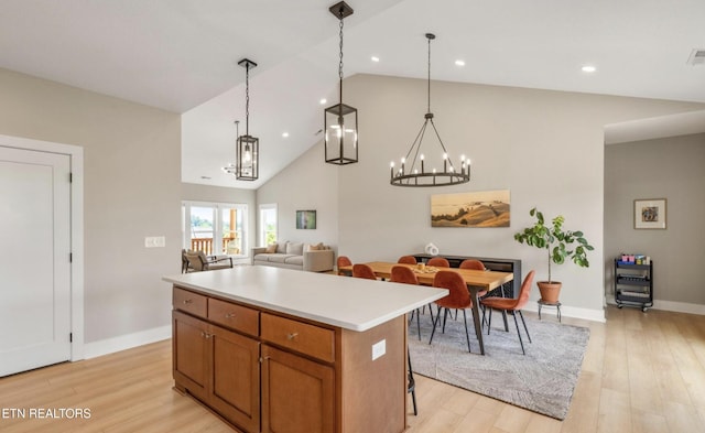 kitchen with high vaulted ceiling, a kitchen island, pendant lighting, and light hardwood / wood-style floors