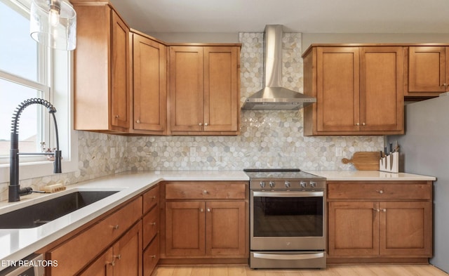 kitchen with wall chimney exhaust hood, sink, tasteful backsplash, stainless steel appliances, and light hardwood / wood-style floors