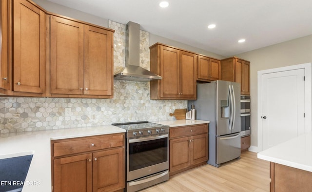 kitchen featuring wall chimney range hood, backsplash, stainless steel appliances, and light hardwood / wood-style floors