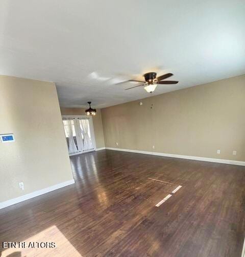 interior space with ceiling fan with notable chandelier, dark wood finished floors, and baseboards