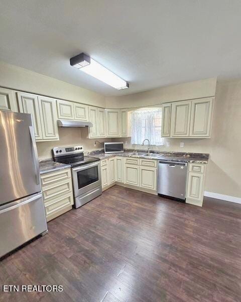 kitchen featuring cream cabinetry, dark wood finished floors, appliances with stainless steel finishes, a sink, and under cabinet range hood