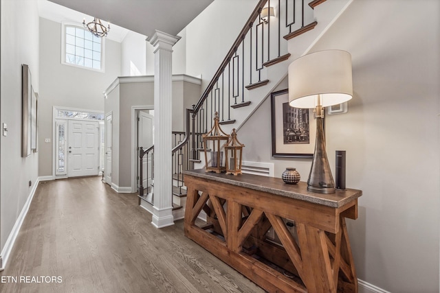 entryway with a notable chandelier, wood-type flooring, a high ceiling, and ornate columns