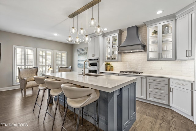 kitchen with premium range hood, a breakfast bar, decorative light fixtures, a center island with sink, and stainless steel appliances