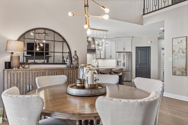 dining room featuring sink, a towering ceiling, wood-type flooring, and a chandelier