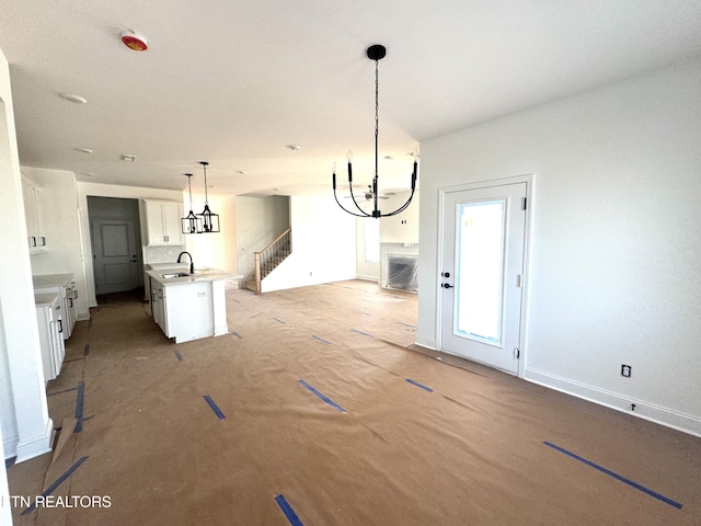 unfurnished dining area with a notable chandelier, a sink, stairway, and baseboards