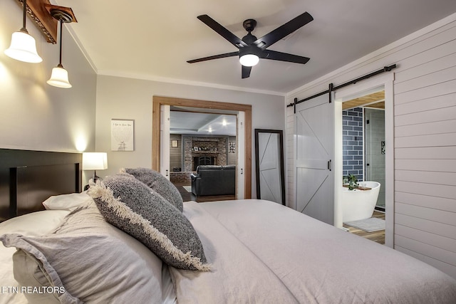 bedroom with crown molding, ensuite bath, a barn door, and a fireplace