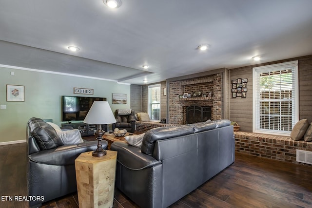 living room featuring dark wood-type flooring, brick wall, and a fireplace