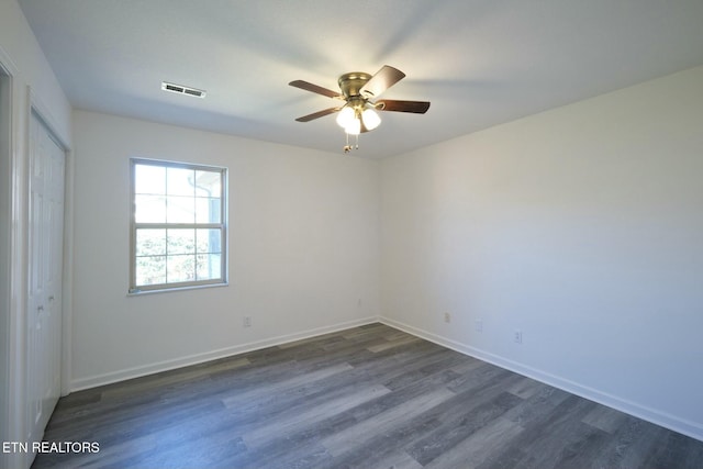 empty room featuring ceiling fan, dark wood finished floors, visible vents, and baseboards