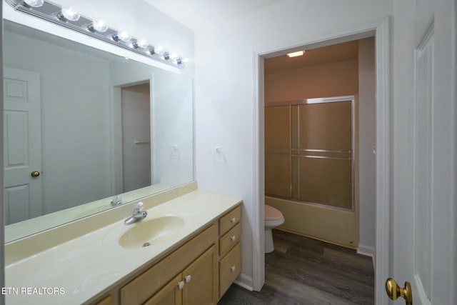 full bath featuring bath / shower combo with glass door, vanity, wood finished floors, and toilet