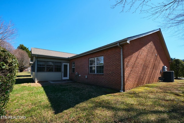 back of property featuring brick siding, a yard, and central AC unit