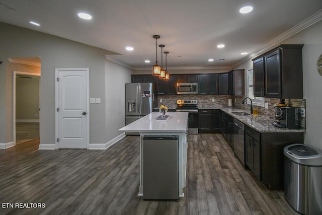 kitchen with pendant lighting, sink, stainless steel appliances, ornamental molding, and a kitchen island