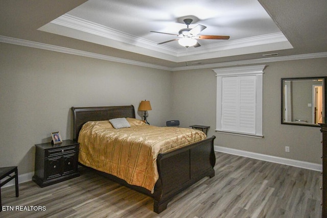 bedroom with dark wood-type flooring, a tray ceiling, and crown molding