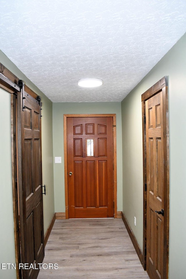 doorway with a barn door, a textured ceiling, and light hardwood / wood-style flooring