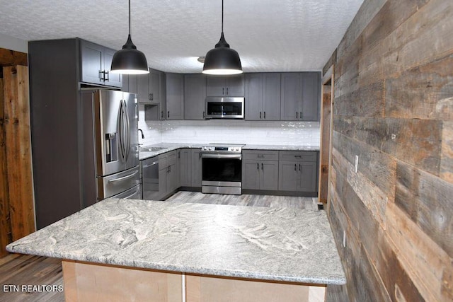 kitchen with stainless steel appliances, gray cabinets, light stone counters, and decorative light fixtures