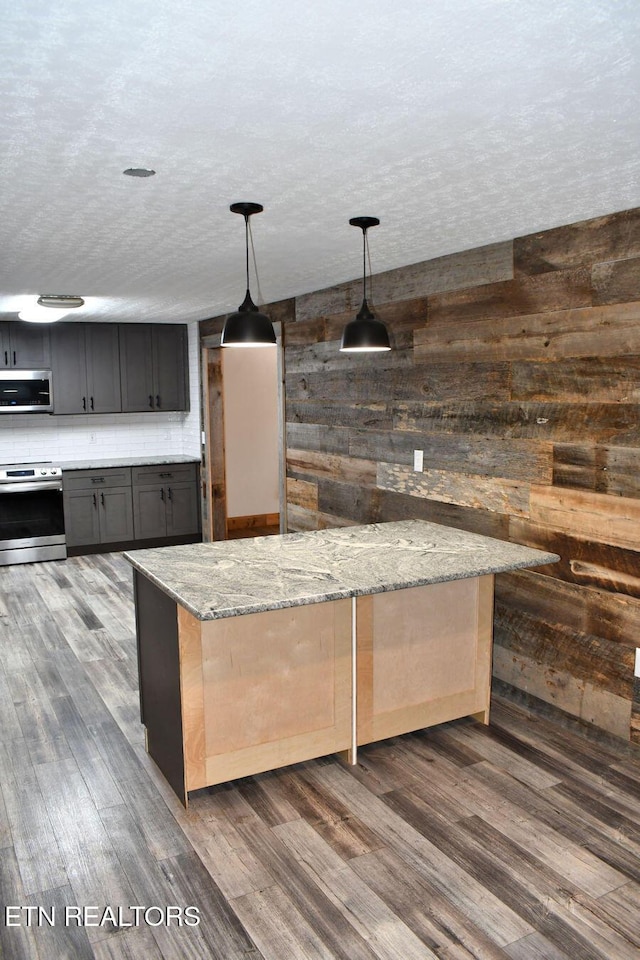 kitchen with dark wood-type flooring, light stone counters, a textured ceiling, pendant lighting, and stainless steel appliances