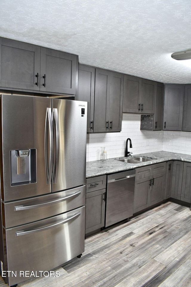 kitchen with sink, decorative backsplash, light stone counters, stainless steel appliances, and light hardwood / wood-style flooring