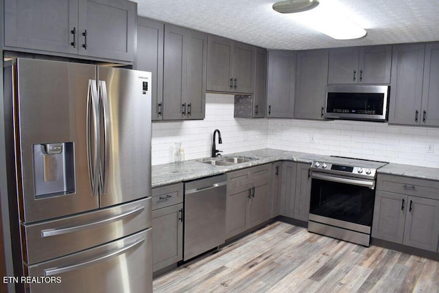 kitchen with gray cabinets, light stone countertops, appliances with stainless steel finishes, and sink