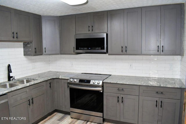 kitchen with stainless steel appliances, light stone countertops, sink, and gray cabinetry