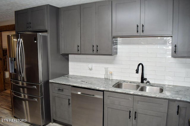 kitchen with appliances with stainless steel finishes, sink, gray cabinetry, backsplash, and light stone counters